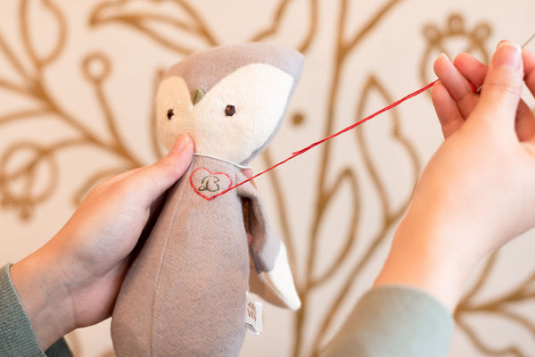 A Hazel Village elf hand embroidering a monogram on an owl doll